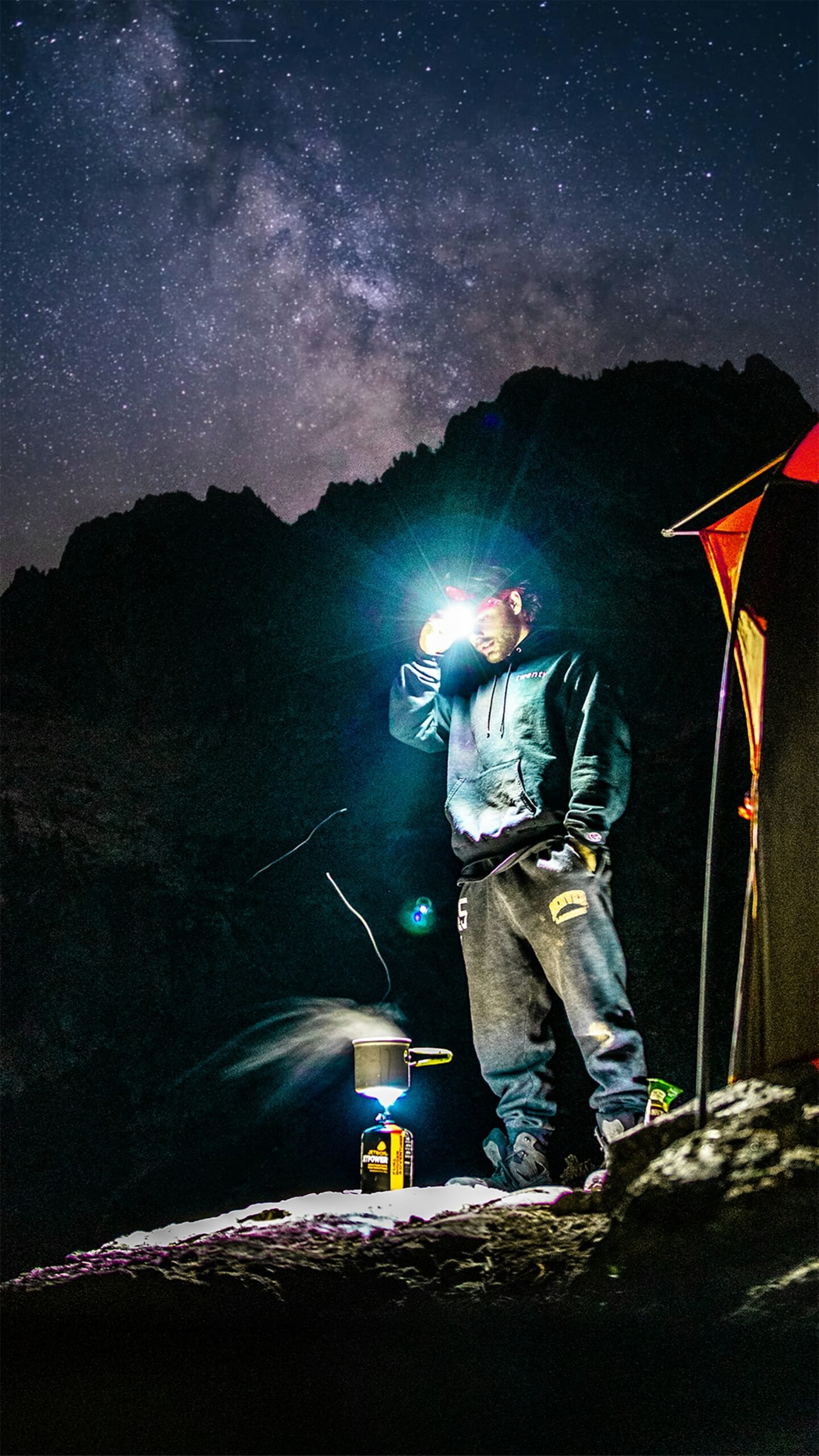 Camper holding flashlight at night near tent